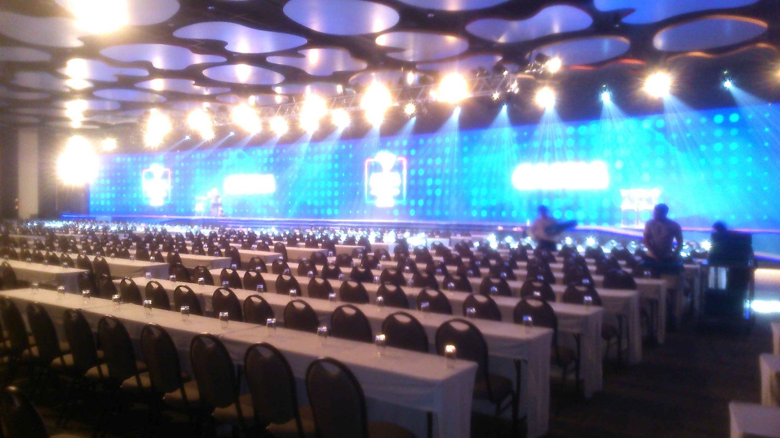 Grande evento corporativo com auditório iluminado e centenas de participantes em votação